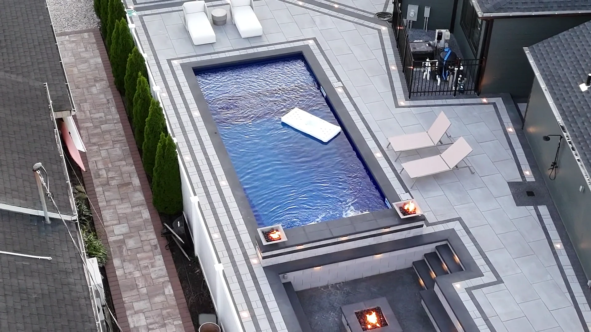 Raised spa with sheer-descent spillway and fire bowls at dusk, Massapequa waterfront
