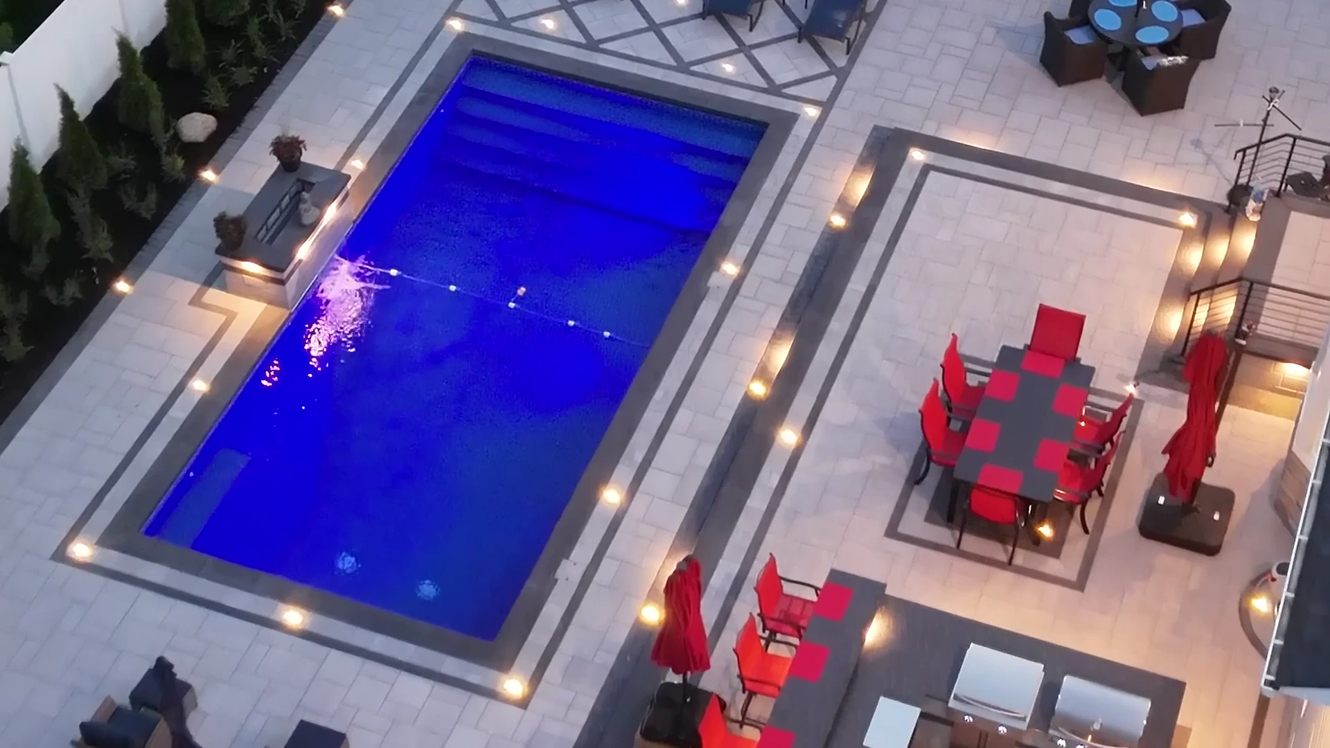 Blue-hour aerial of the finished lit pool, spa and paver deck in Nesconset, Long Island