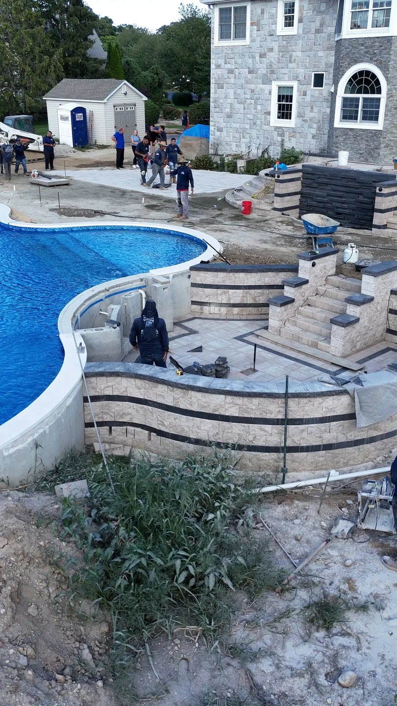 Retaining walls and stepped hardscape under construction around the pool shell, East Northport