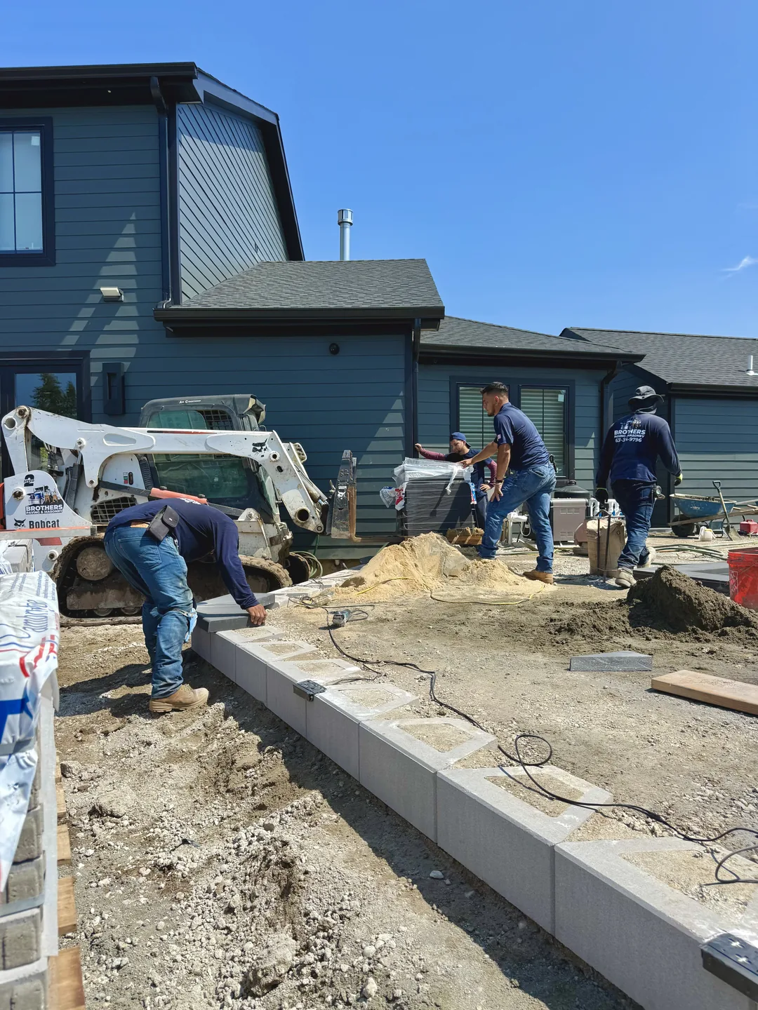 Brothers Paving & Masonry crew in branded uniform setting pavers over the compacted base on the Massapequa site