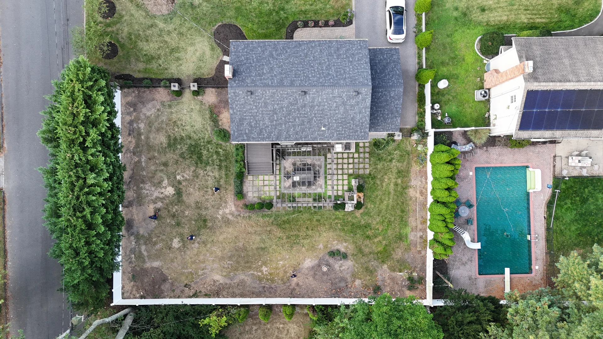 Overhead of the bare rear yard before construction, with patchy lawn and a small grid-paver patio, Nesconset