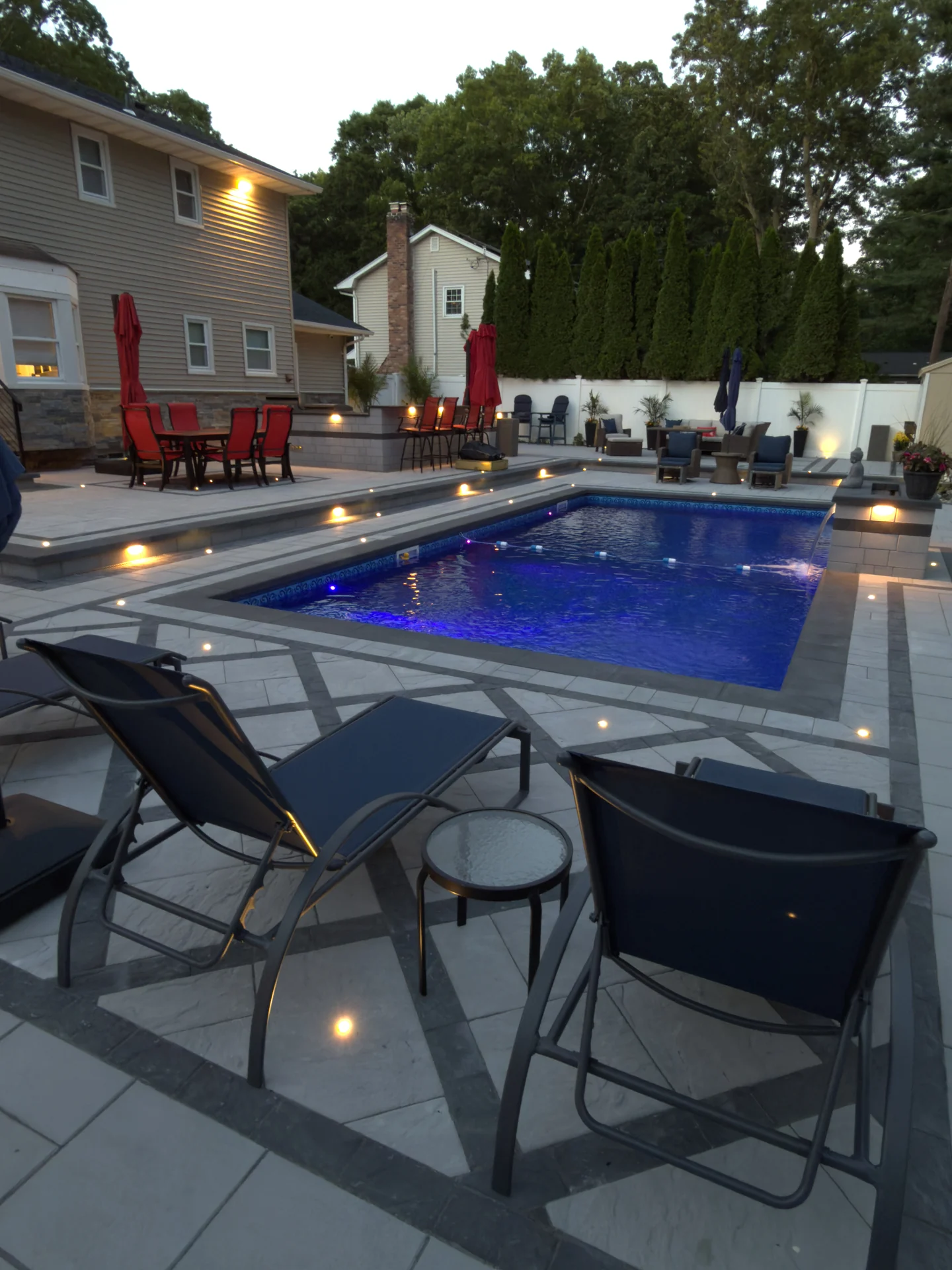 Loungers on the paver deck beside the lit pool, Nesconset