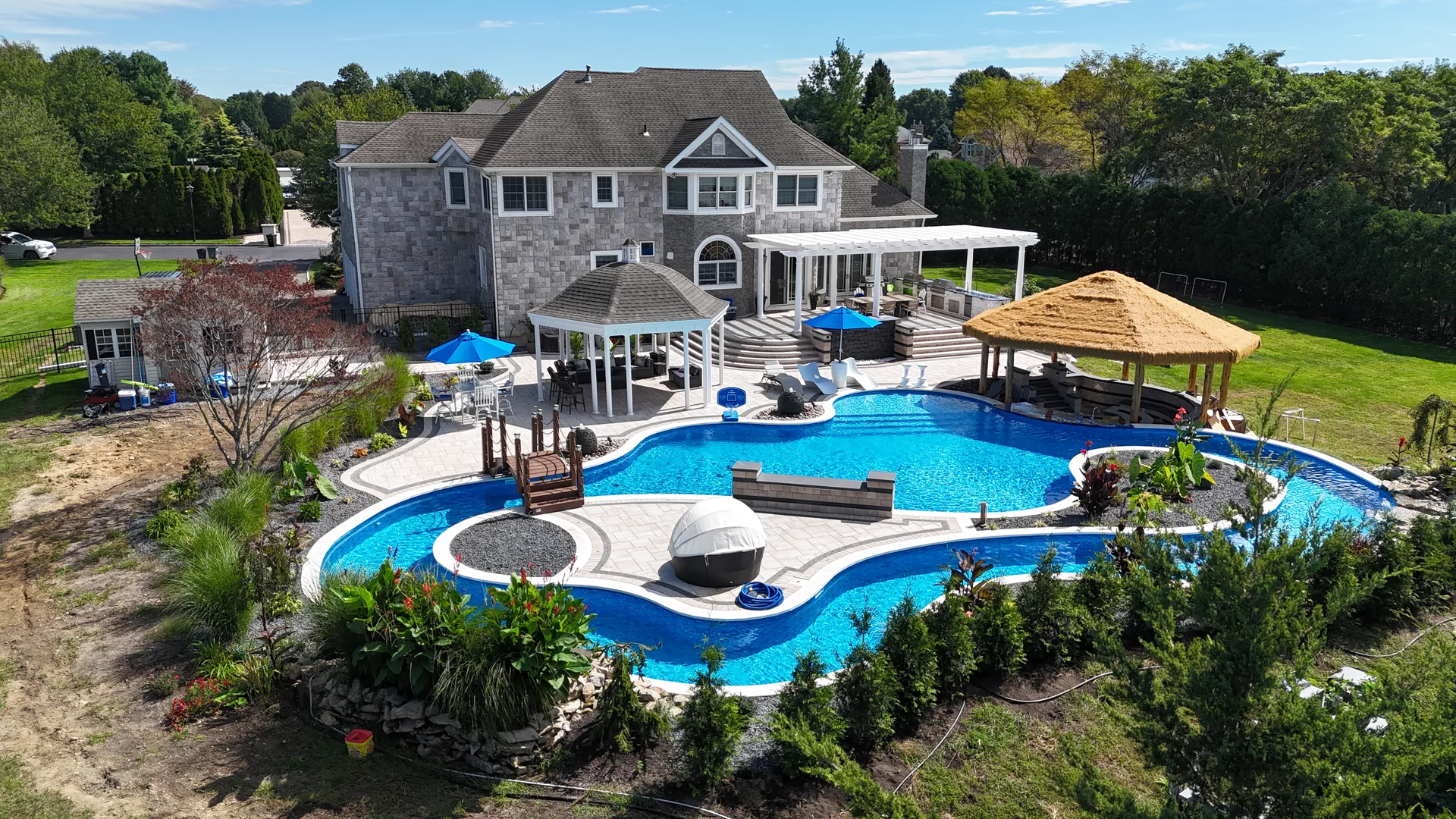 Aerial of the full property — house, lazy river, planted island and palapa — in East Northport, Long Island