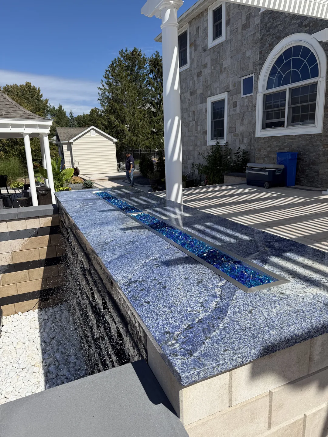 Sheer-descent water wall set into banded stone veneer beside the pool, East Northport