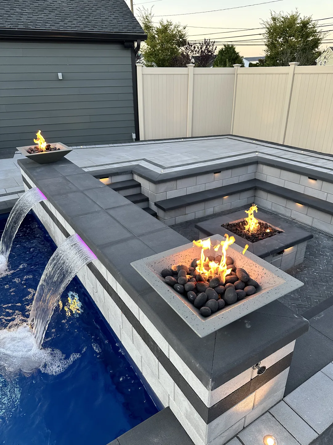 Raised spa with sheer-descent spillway and fire bowls at dusk, Massapequa waterfront