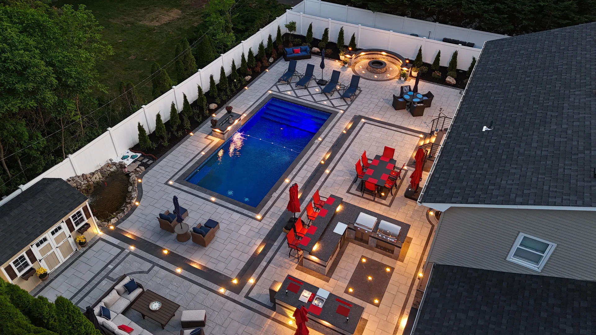 Blue-hour aerial of the lit pool, spa and surrounding deck, Nesconset