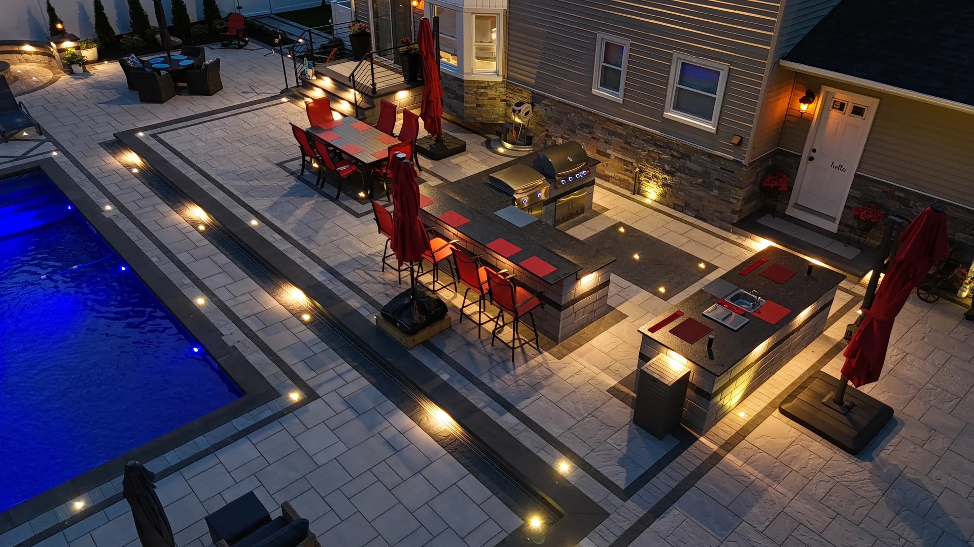 The kitchen, dining terrace and pool lit together at dusk, Nesconset